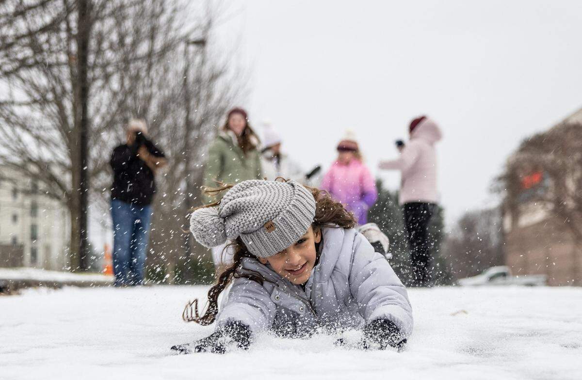 Kylie Fernandez, of Ocala, FL, slides on her belly through the snow in a parking lot in Charlotte in January 2022.