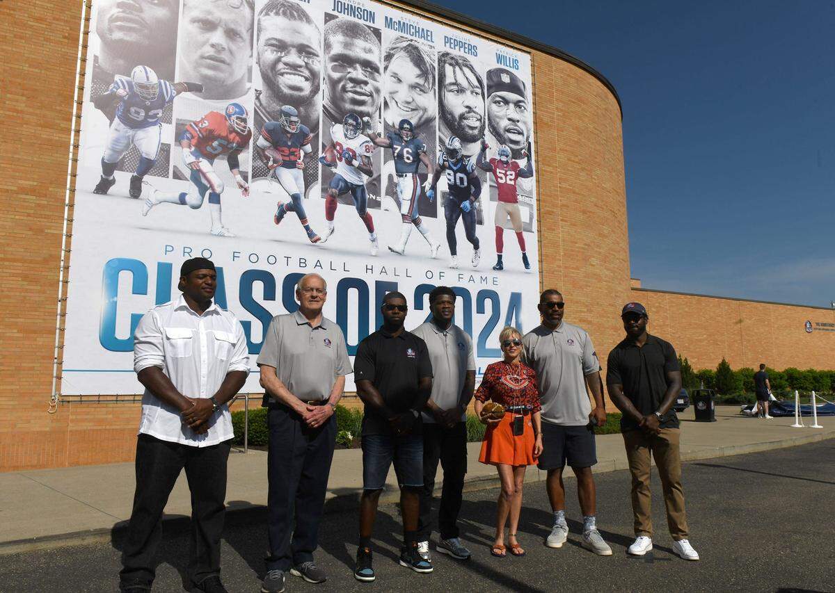 The Pro Football Hall of Fame Class of 2024 (from left) of Dwight Freeney, Randy Gradishar, Devin Hester, Andre Johnson, Misty McMichael (representing husband Steve McMichael), Julius Peppers and Patrick Willis unveil the class banner at the Hall, Friday, May 24, 2024.
