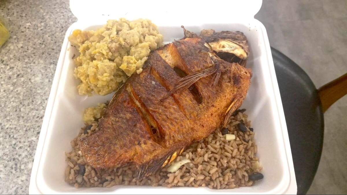 A white styrofoam takeout container filled with a large portion of yellow seasoned rice (arroz con gandules), shredded slow-roasted pork (pernil), and several pieces of fried sweet plantains (maduros).