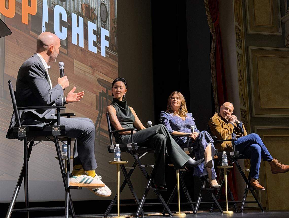 An interior, eye-level shot captures four people sitting in chairs on a stage during a panel for “Top Chef,” as indicated by the logo on the screen behind them.