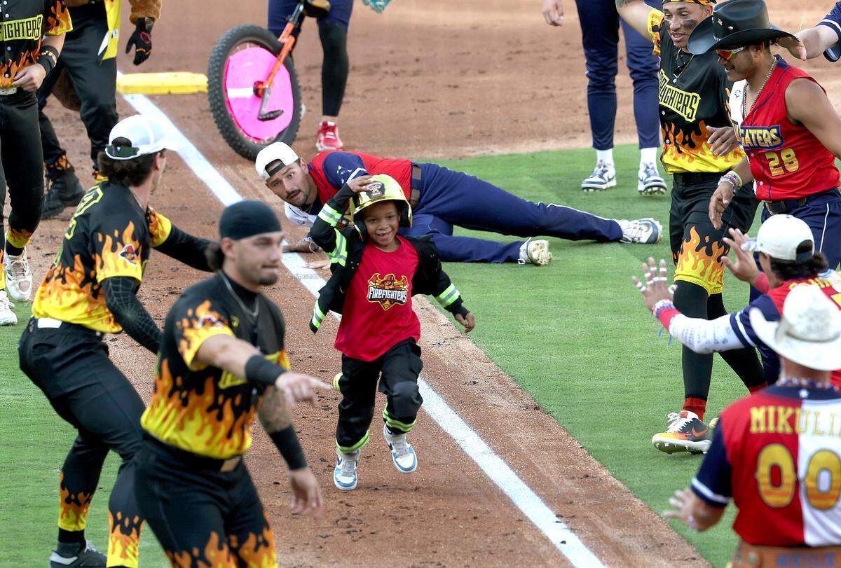A young fan holds onto his helmet as he runs to home plate with members of the Texas Tailgaters and Firefighters looking on during pregame festivities at Truist Field in Charlotte, NC on Thursday, June 4, 2026. Banana Ball action returned to the Queen City with the Texas Tailgaters battling the Firefighters.