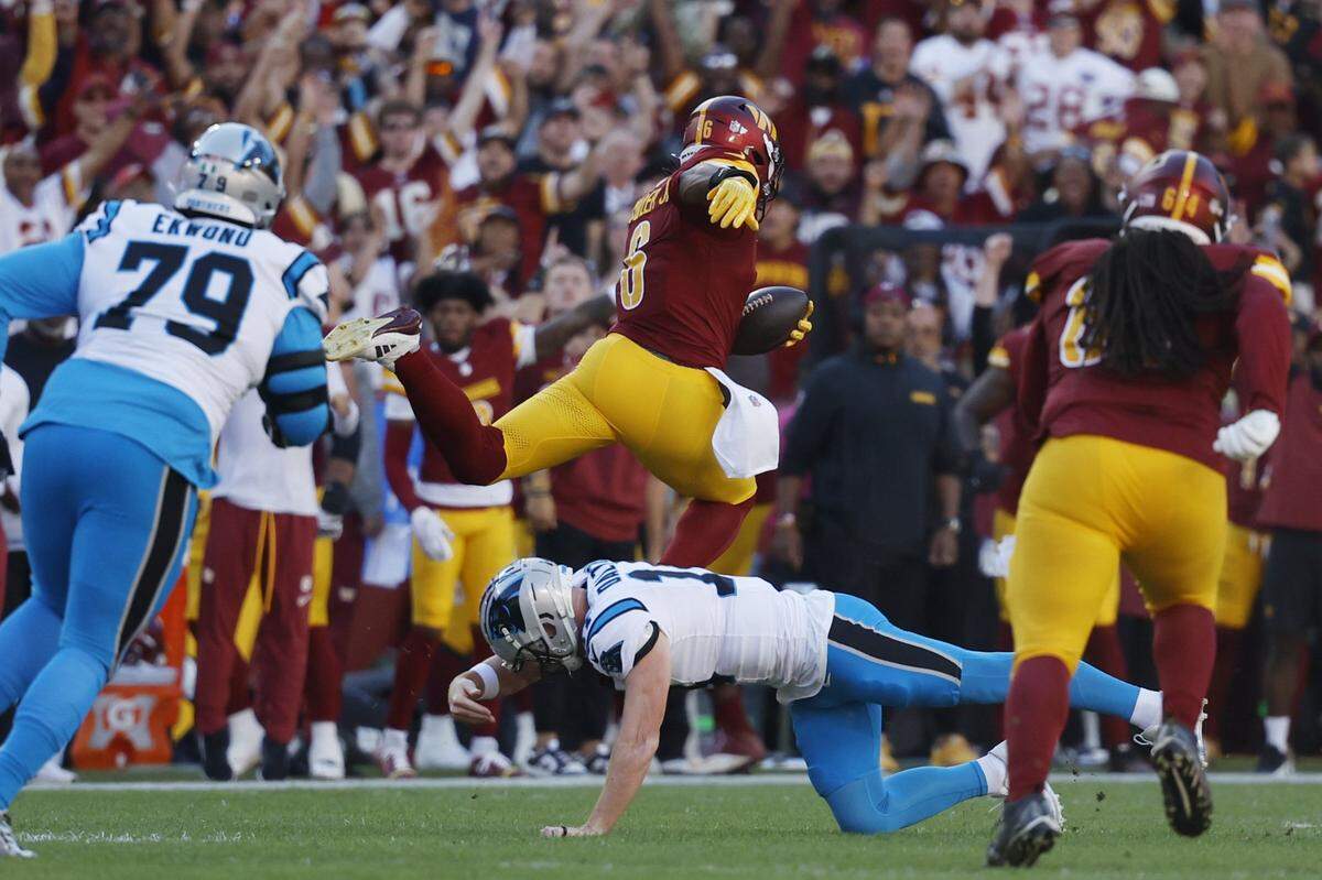 Oct 20, 2024; Landover, Maryland, USA; Washington Commanders linebacker Dante Fowler Jr. (6) leaps over Carolina Panthers quarterback Andy Dalton (14) after intercepting a pass en route to a touchdown during the first quarter at Northwest Stadium. Mandatory Credit: Geoff Burke-Imagn Images