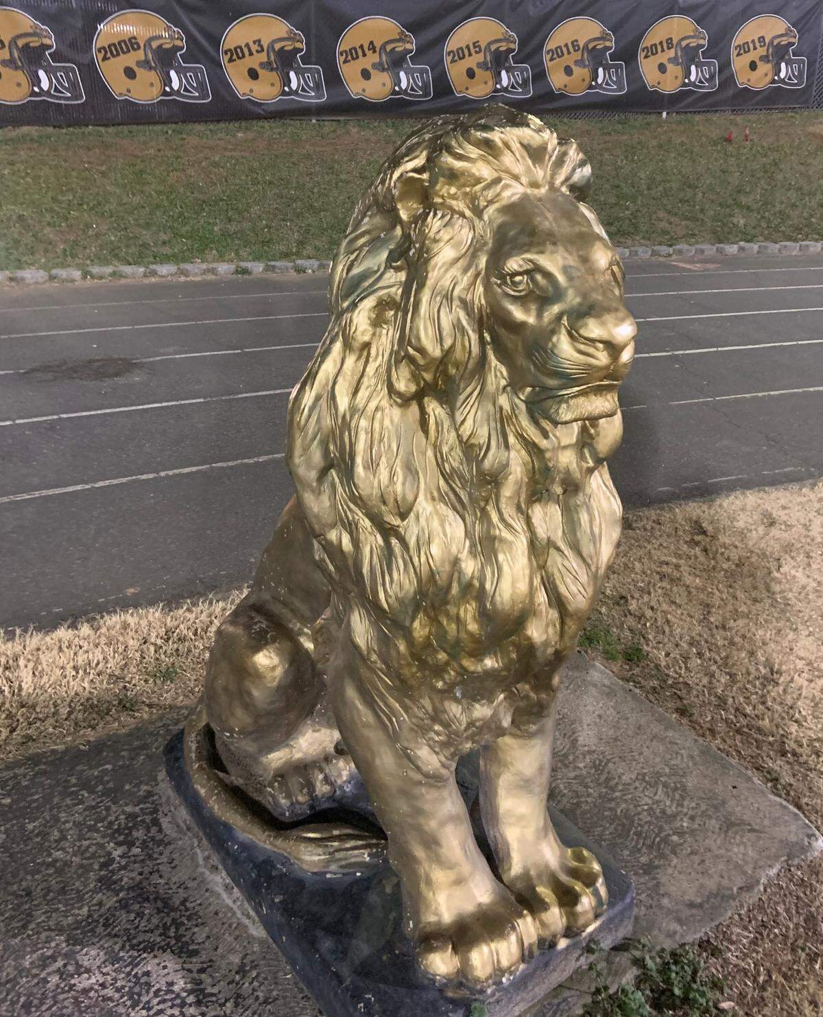 A statue of a golden lion sits in front of the Shelby High School Football field, with helmets displaying some of the years that the school has won football state championships in the background. The Golden Lions have won six state titles in the past eight years heading into Saturday’s championship game on Dec. 11, 2021, vs. Wallace-Rose Hill in Raleigh.