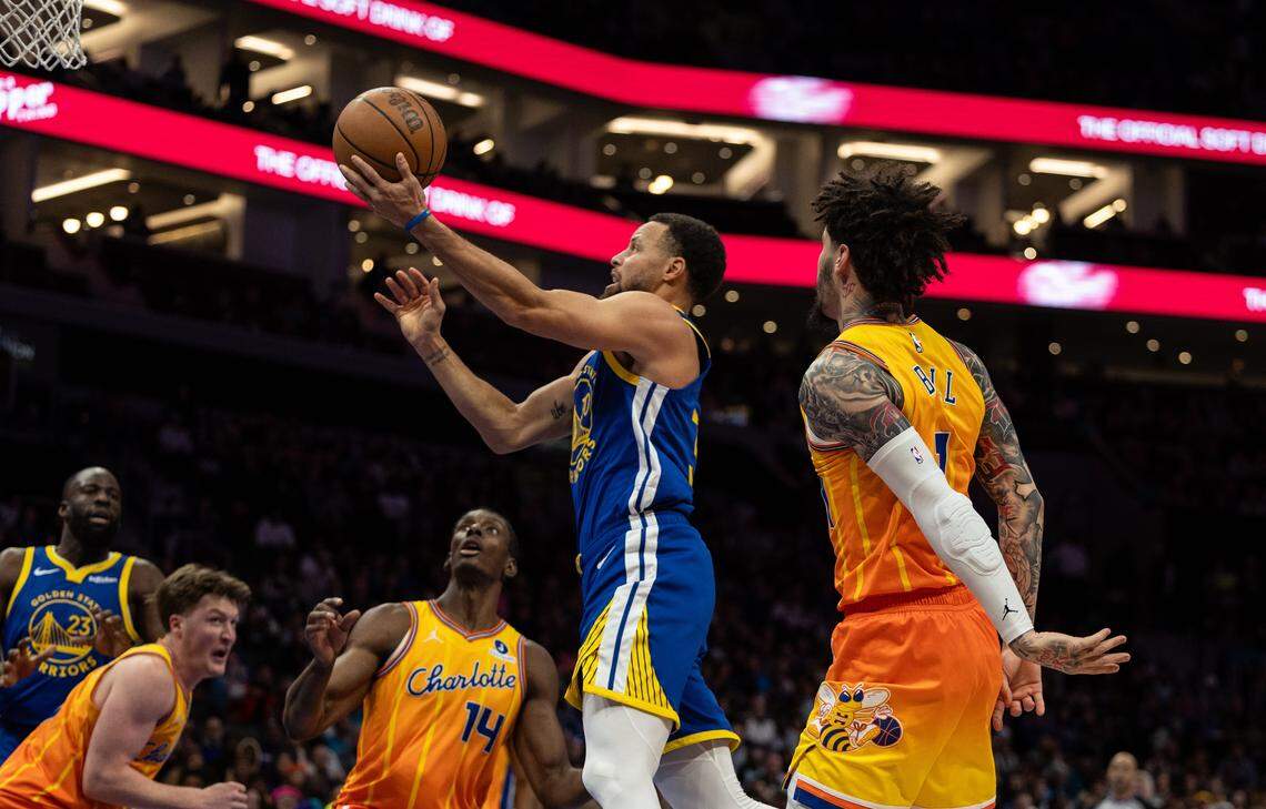 Golden State Warriors guard Stephen Curry, center, shoots past Charlotte Hornets guard Lamelo Ball on Dec. 31, 2025, at the Spectrum Center in Charlotte. Curry scored 26 points in Golden State’s 132-125 win before a sellout crowd.