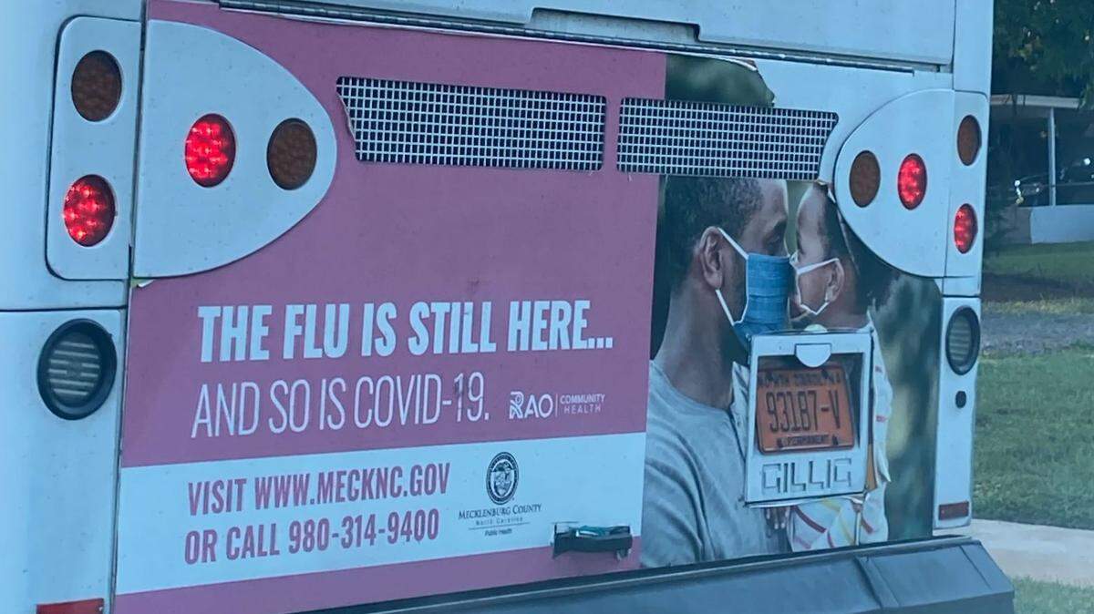 An ad on the back of a CATS bus from the Mecklenburg County Health Department appears to show a father and son embracing each other while wearing masks.