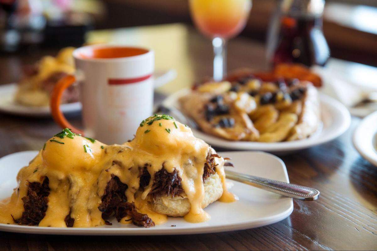 A close-up of a brunch dish featuring pulled pork on a biscuit, covered in a creamy yellow sauce and garnished with chives.