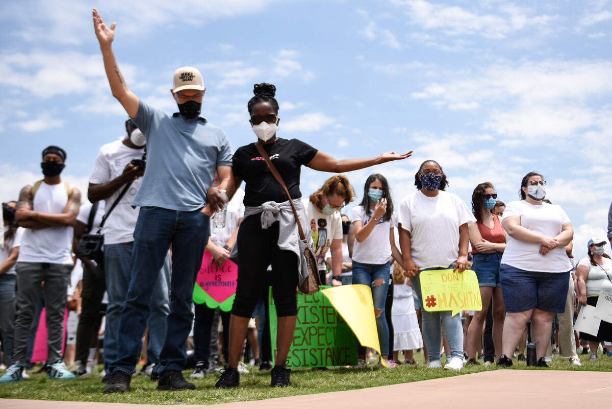 Two demonstrators raise their hands as they listen to a song about lives lost to police brutality in First Ward Park on May 31, 2020, during an It Ends Now Charlotte rally.