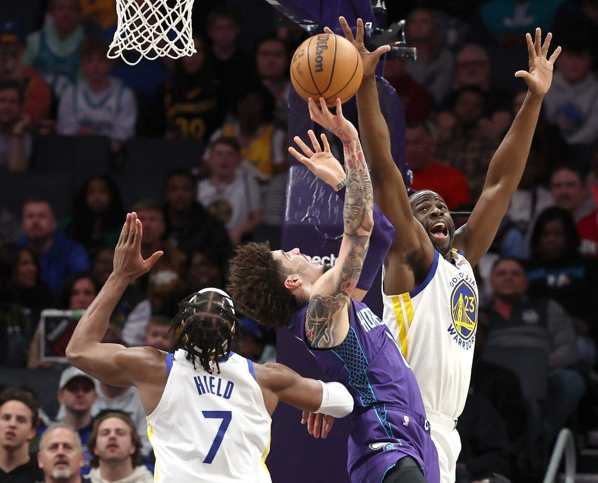 Charlotte Hornets guard LaMelo Ball, center, fights to get a shot up in the lane as Golden State Warriors forward/center Draymond Green, right, applies defensive pressure during action at Spectrum Center in Charlotte, NC on Monday, March 3, 2025.