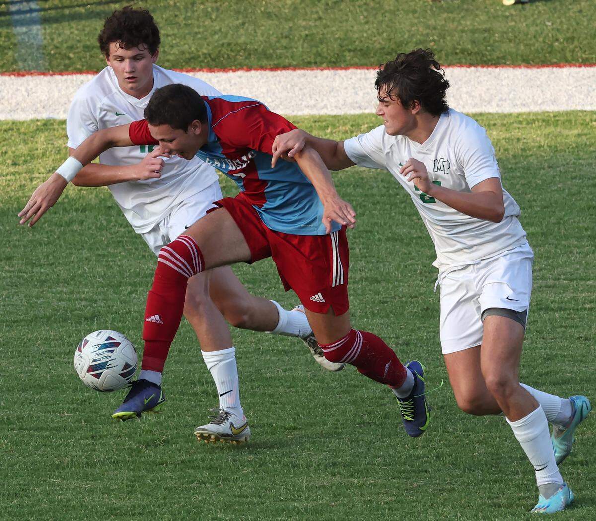 Charlotte Catholic’s Mason Poveromo, center, pushes the ball between two Myers Park’s defenders during the season opening match at Charlotte Catholic School on Monday, August 14, 2023.