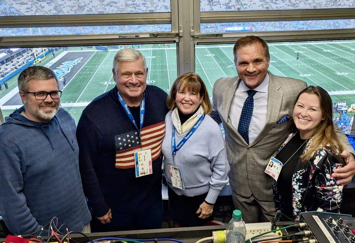 Bill Rosinski (in American flag sweater), surrounded by colleagues and family, at the Carolina-Seattle game in Charlotte in December 2025. Rosinski called the game for Compass Media Net, one of two Panthers games he worked last season.
