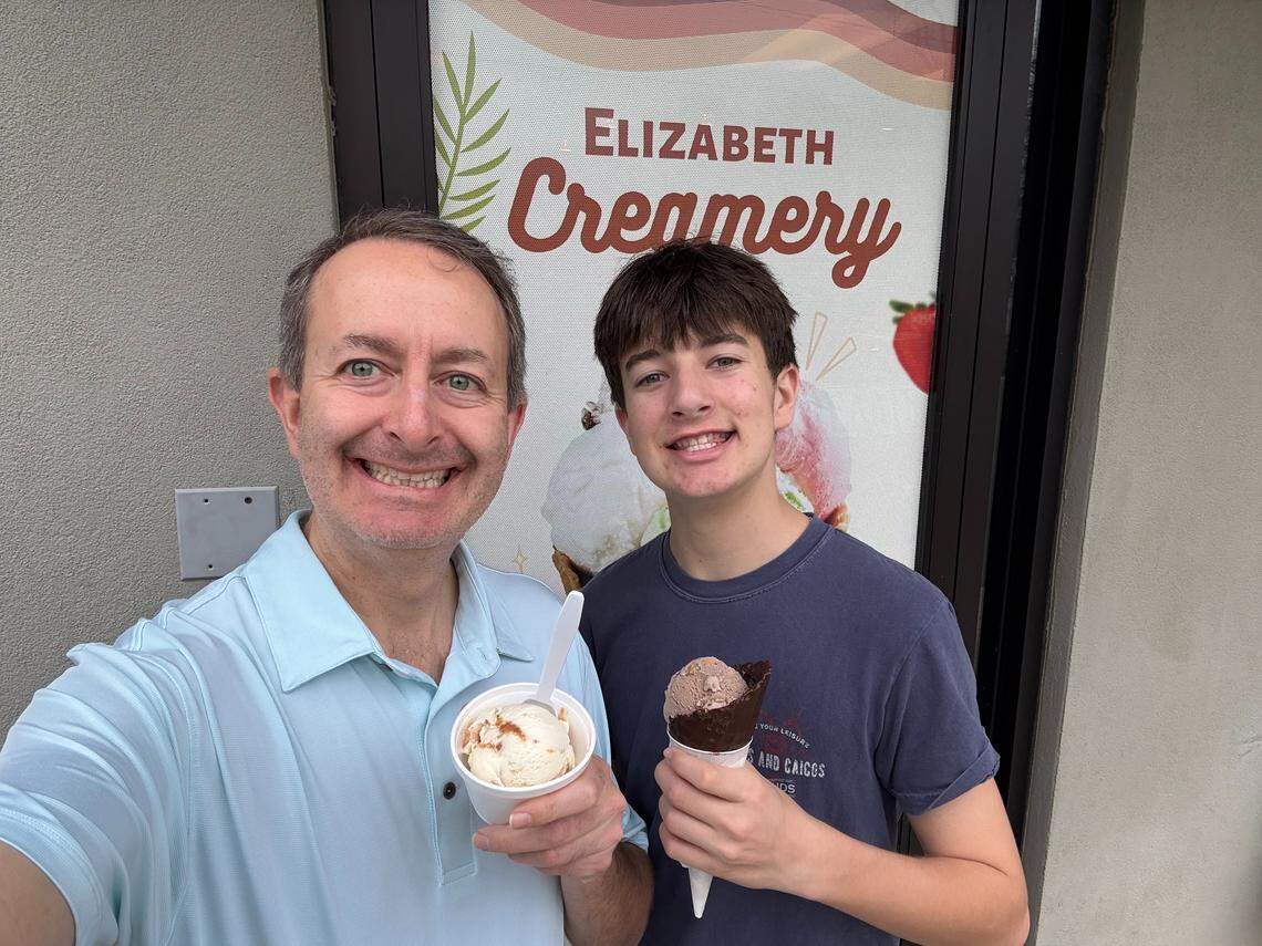 A selfie of a two people, one older and one younger, smiling outside Elizabeth Creamery. The older person holds a white cup of ice cream and the younger holds a chocolate-dipped waffle cone.
