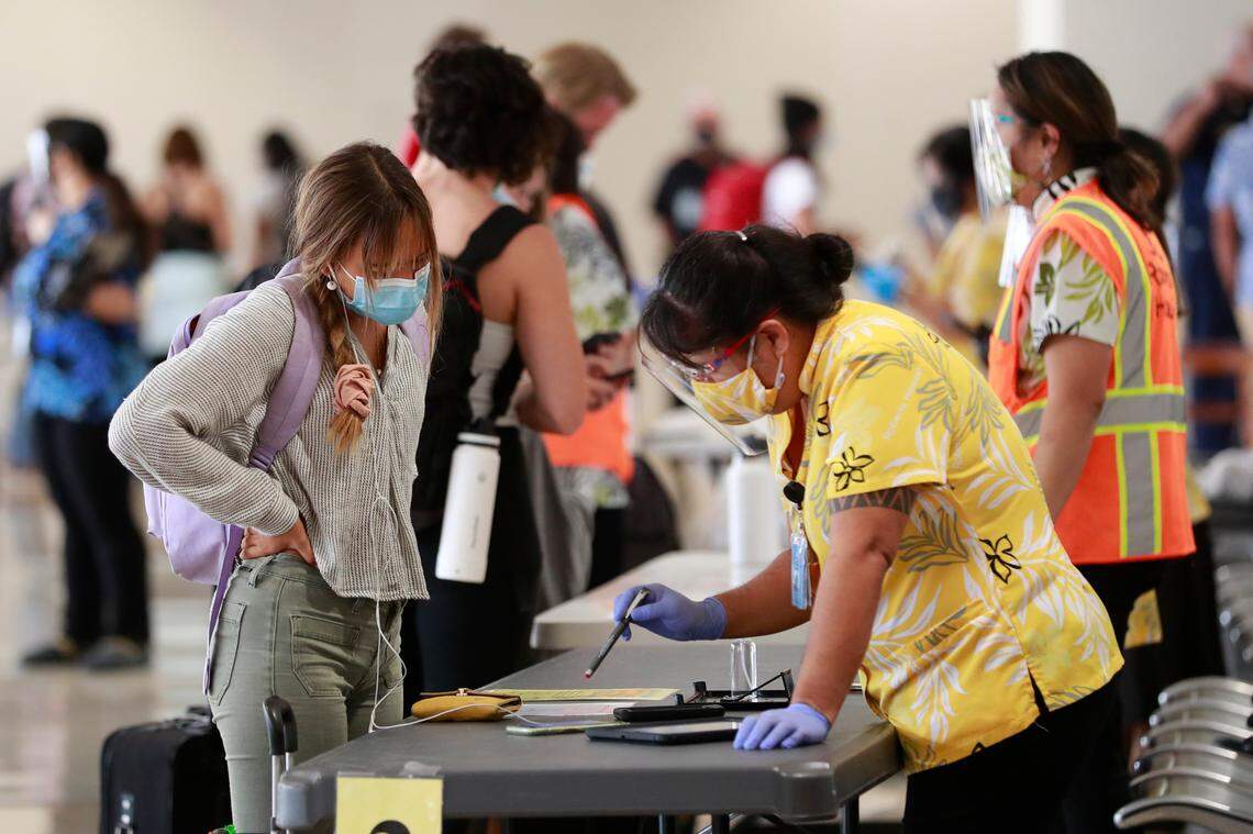 A state official assists a traveler at the Daniel K. Inouye International Airport on Thursday, Oct. 15, 2020, in Honolulu. Travelers “are subject to” Hawaii’s mandatory 10-day self-quarantine without a valid negative COVID-19 test by a company on the state’s “Trusted Testing and Travel Partners” list.