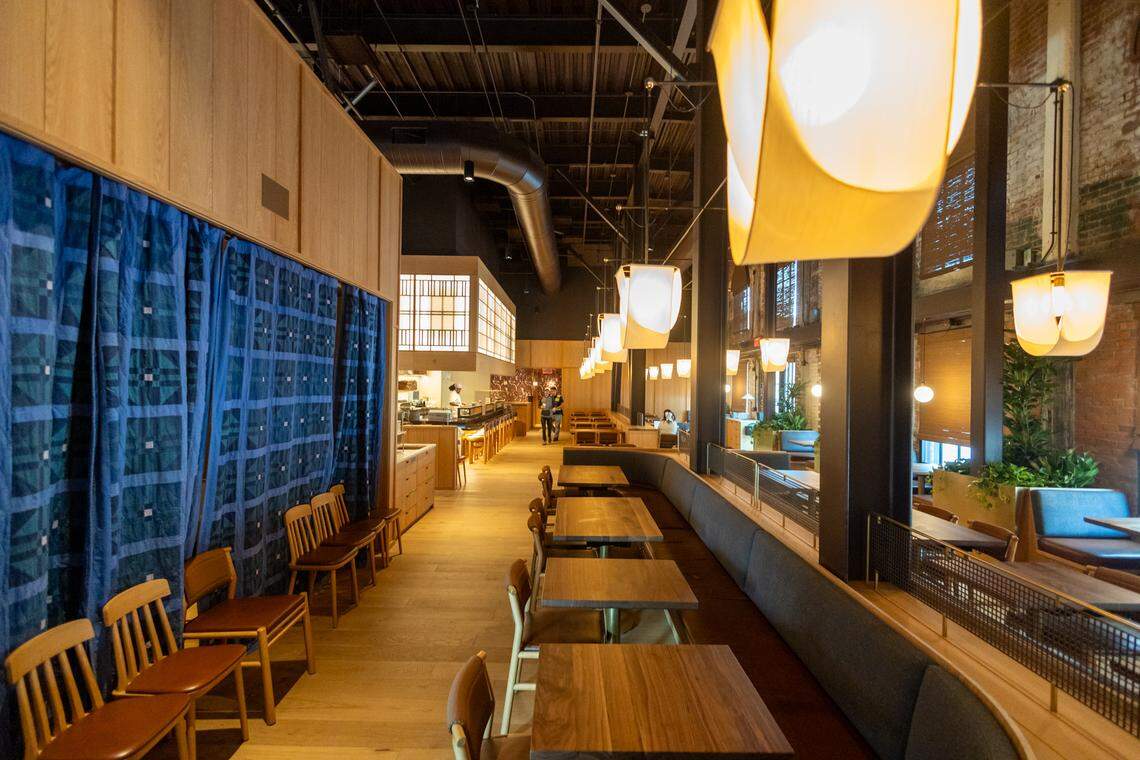 The interior is characterized by a mix of geometric patterns, natural wood, and industrial architecture. A prominent L-shaped bar serves as a focal point, featuring a dark countertop and a base tiled in a cream and tan triangular geometric pattern.