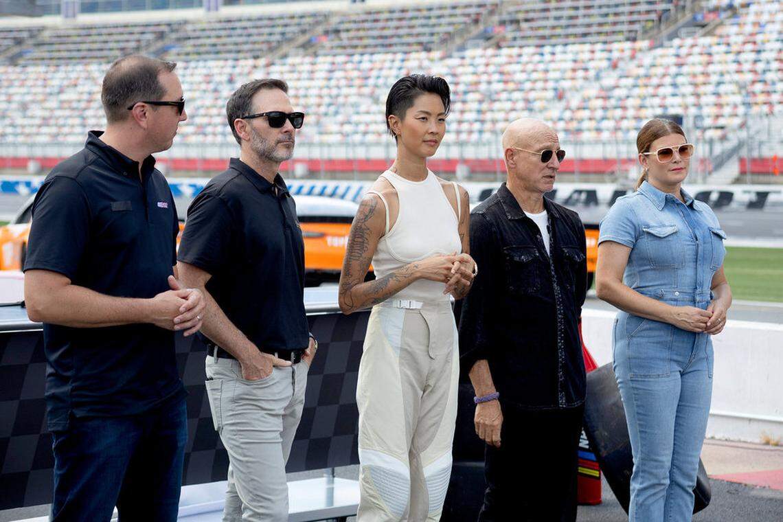 Three television chefs stand along with two race car drivers near the race track at Charlotte Motor Speedway.