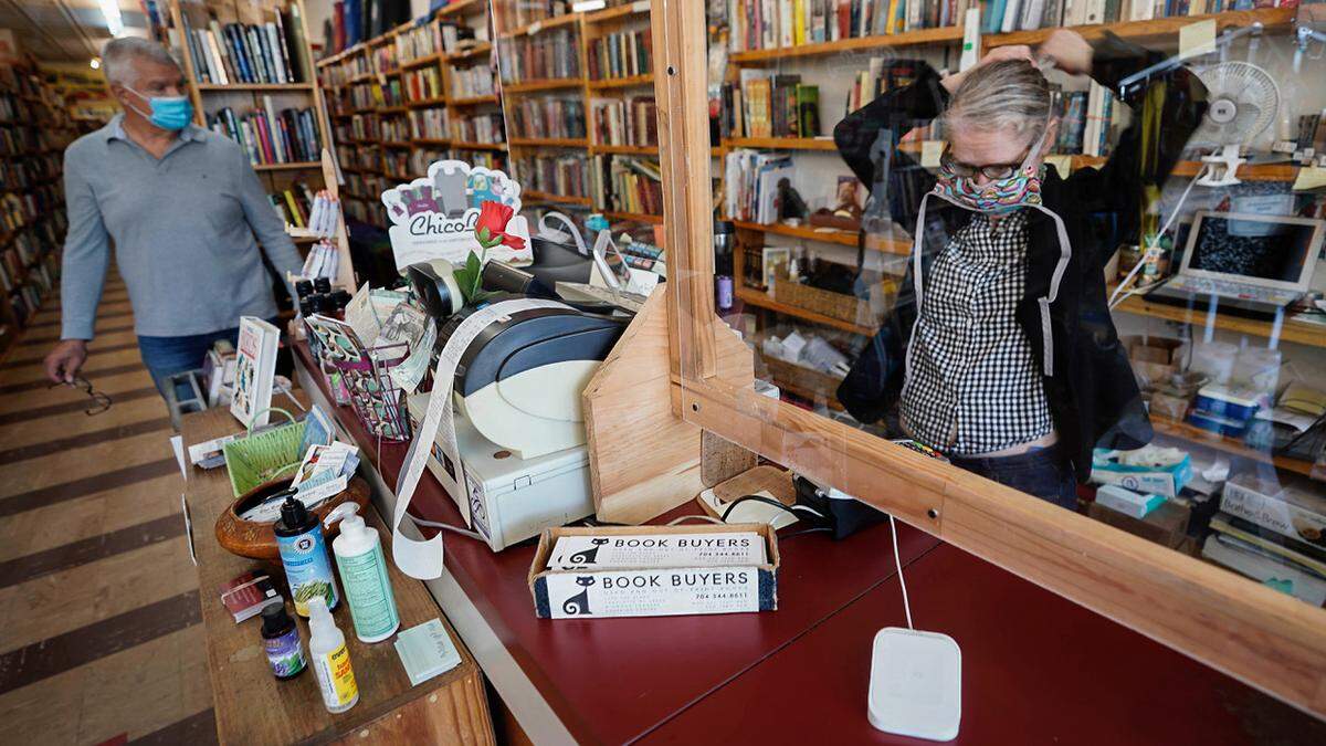 Lee Rathers, right, of Book Buyers ties her mask as she prepares to help a customer on  May 11, 2020, as part of  Phase 1 reopening of merchants in North Carolina.