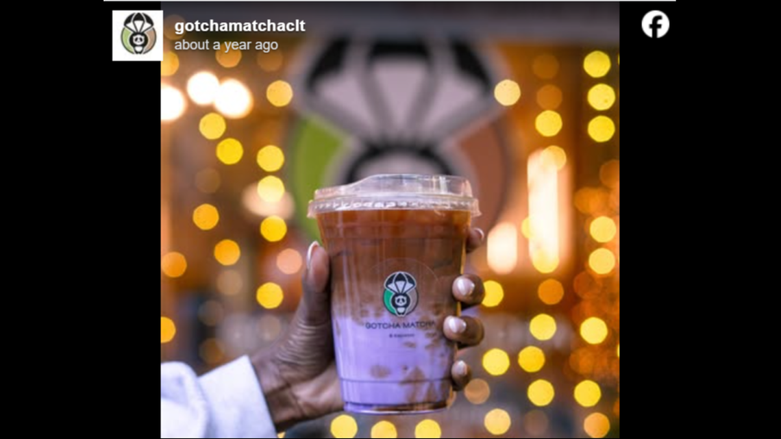 A person’s hand holds a layered iced beverage from Gotcha Matcha, featuring a purple base topped with dark coffee or tea. The background is filled with warm, glowing bokeh lights and the shop’s panda logo is visible on the clear plastic cup.