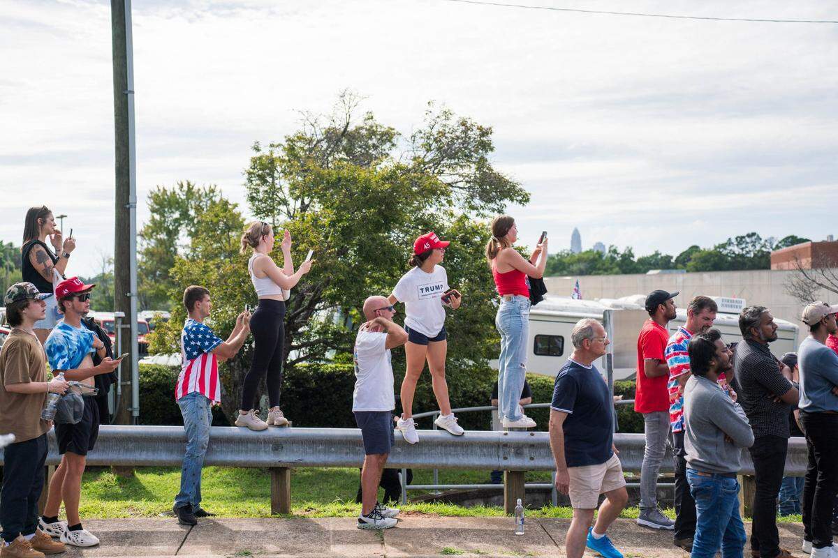Trump supporters standing on the side of the road to try and get a glimpse of the former President Donald Trump as he is arriving in his motorcade before the rally at the Bojangles Coliseum in Charlotte on July 24, 2024.