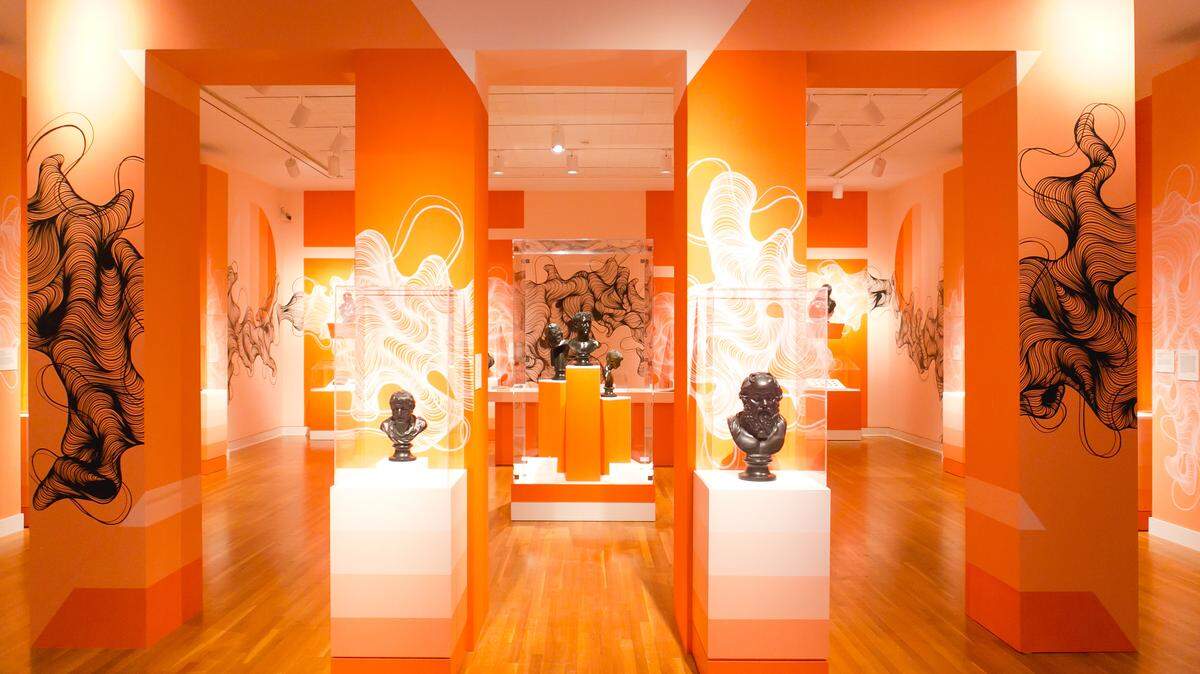 The setting for the Mint Museum’s latest exhibit, “Classic Black: The Basalt Sculpture of Wedgwood and His Contemporaries,” may surprise some visitors. A local artist’s line drawings adorn walls and columns throughout the galleries and the sunset hues of the walls complement the black basalt sculptures.