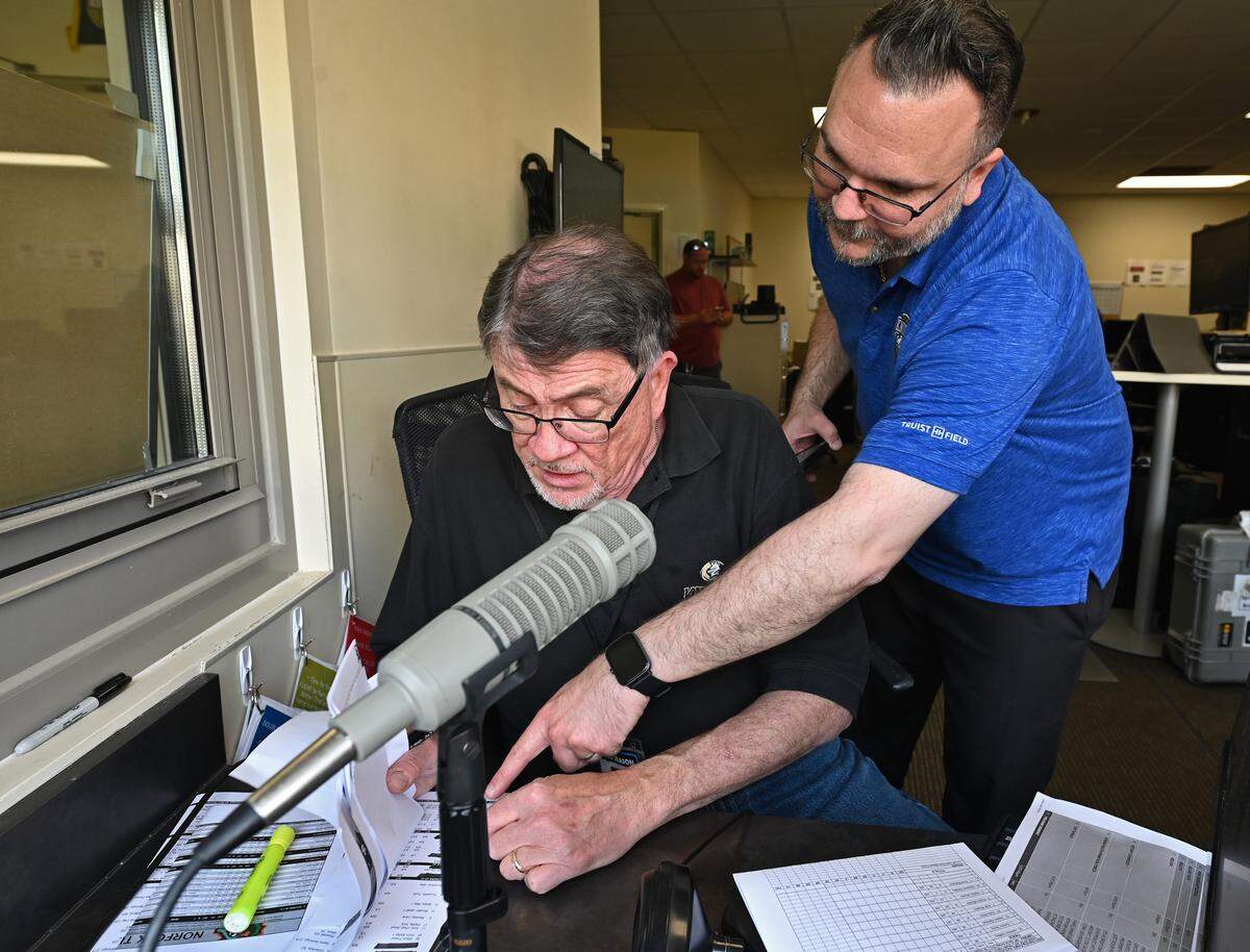 Charlotte Knights public address announcer Ken Conrad, left and Tommy Viola, right, the Vice President of Communications look over the rosters for the team’s home opener against the Norfolk Tides on Tuesday, April 2, 2024 at Truist Field in Charlotte, NC. Conrad has been with the team for 23-years.