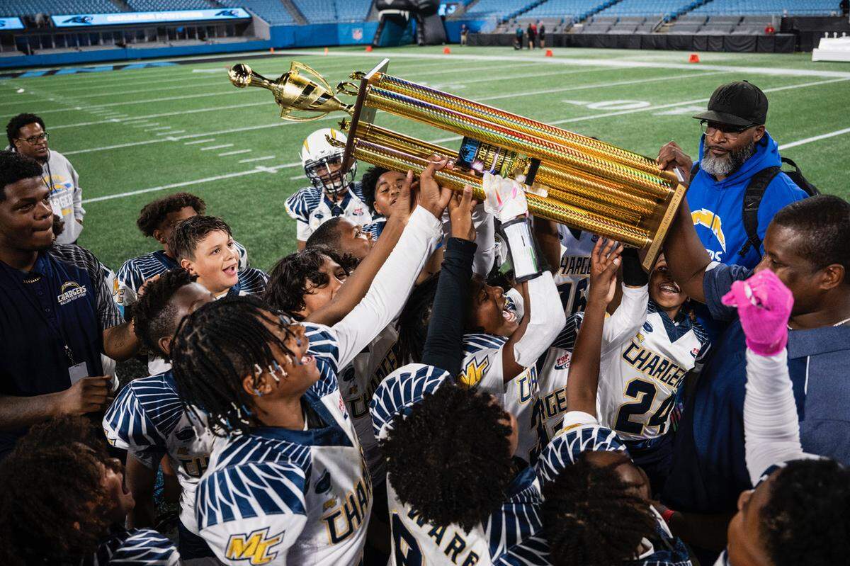 Mallard Creek Chargers head coach, Arthur Jones (carrying trophy, right), celebrates with his team after defeating the MARA Colts on a special, historic night in Bank of America Stadium on Monday, Oct. 30, 2023.