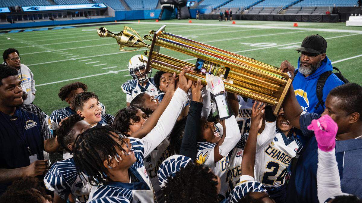 Mallard Creek Chargers head coach, Arthur Jones (carrying trophy, right), celebrates with his team after defeating the MARA Colts on a special, historic night in Bank of America Stadium on Monday, Oct. 30, 2023.
