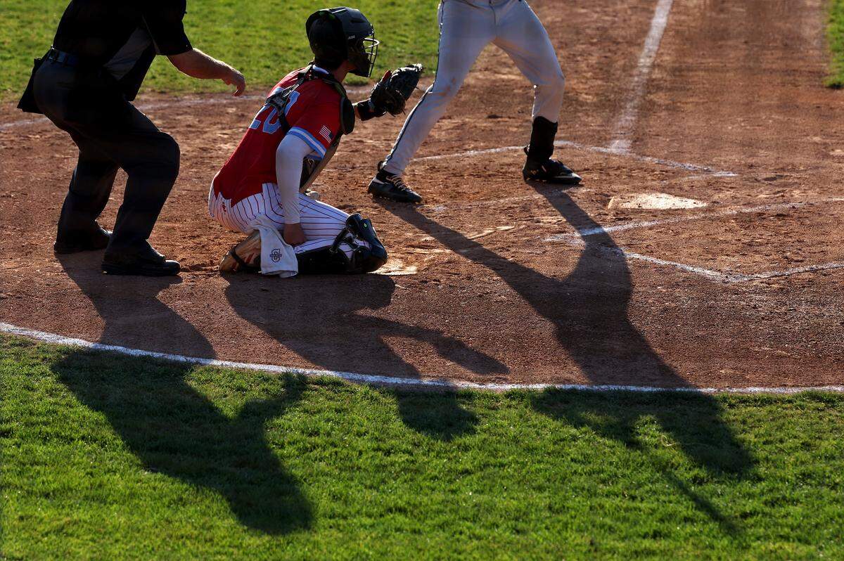 The shadows of the umpire, Charlotte Catholic Cougars catcher Brady Marconi and an AC Reynolds batter are cast onto the filed during third round NCHSAA action at Jack Hughes Park in Pineville, NC on Tuesday, May 12, 2026. AC Reynolds defeated Charlotte Catholic 5-4.