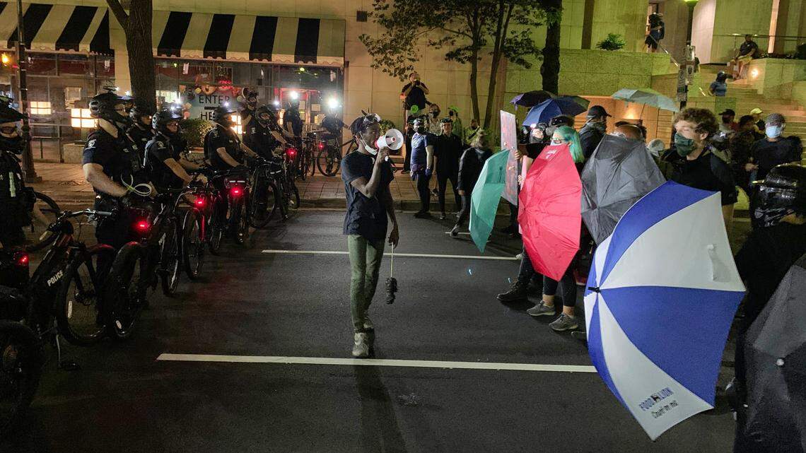 Police officers with their bicycles form a line opposite of protesters with open umbrellas in downtown Charlotte Saturday night, Aug. 22, 2020.