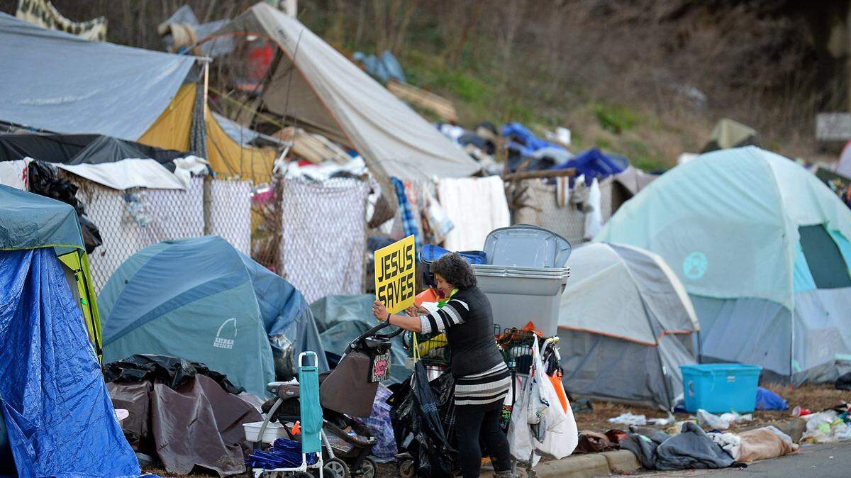 A woman places the Jesus Saves sign among her personal items at the tent encampment along 12th Street in Charlotte, NC on Friday, February 19, 2021. Residents of tent encampment are being vacated after health risks from rodent infestation was found in the area.