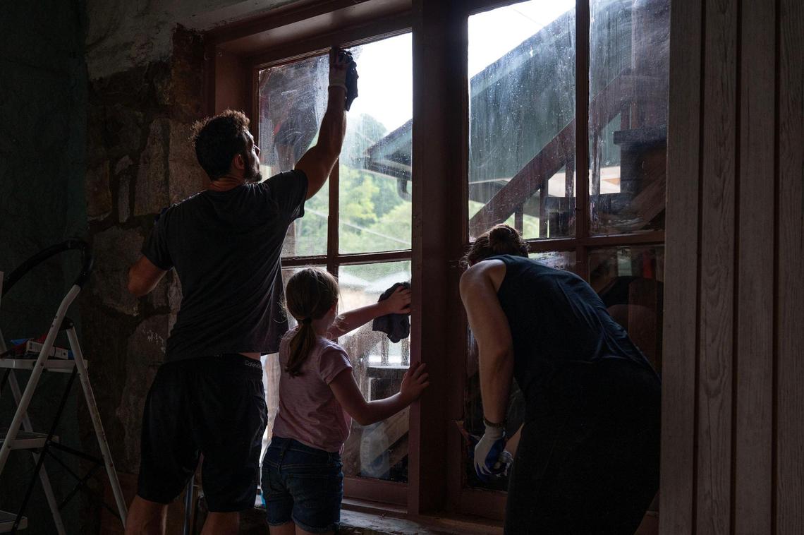 The Kulak family scrapes and washes away paint residue from the windows of the building they are repairing in Chimney Rock.