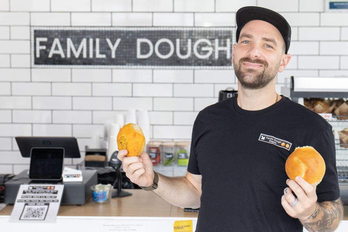 The owner of Family Dough Bagels holding a bagel in each hand.