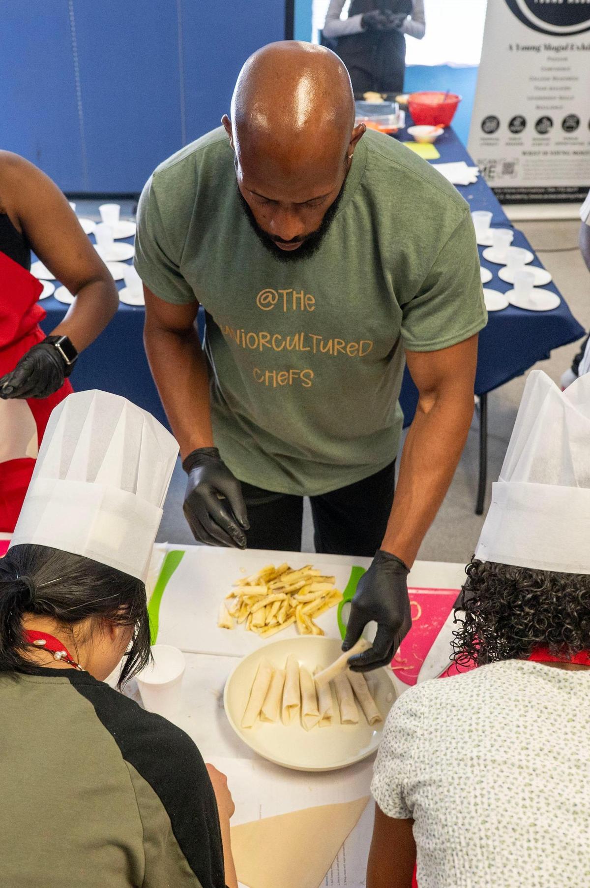 Chef Jon Rhodes demonstrates to students how to make the dessert dish of bananas wrapped in puff pastry during the ‘Can U Cook?’ cooking class segment of the Young Moguls’ Summer Camp at A.C.E. Academy in Harrisburg, NC, Tuesday June 17, 2025. Jon Rhodes founded ‘Can U Cook?’ with Chef Gillian Howard which includes ‘The Junior Cultured Chefs’ camps for children.