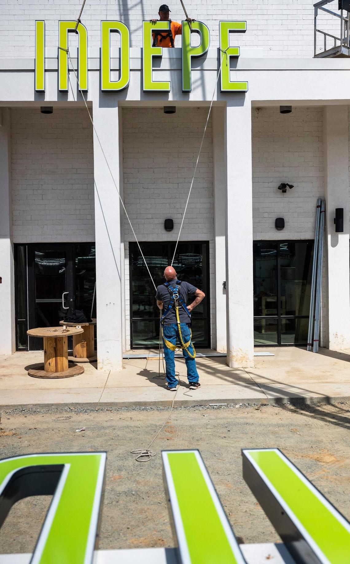 Jim Petty, bottom, and Gary Blanton, with Gary’s Signs, work on securing the first half of the sign to the building’s facade for the Charlotte Film Society’s Independent Picture House on Tuesday, March 22, 2022 in Charlotte.