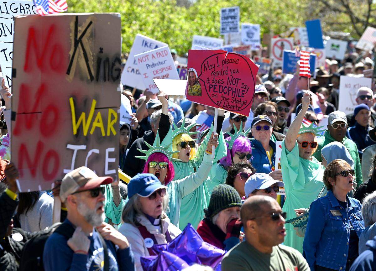 Protesters hold their signs high as they cheer speakers in First Ward Park during a No Kings rally in Charlotte, NC on Saturday, March 28, 2026.
