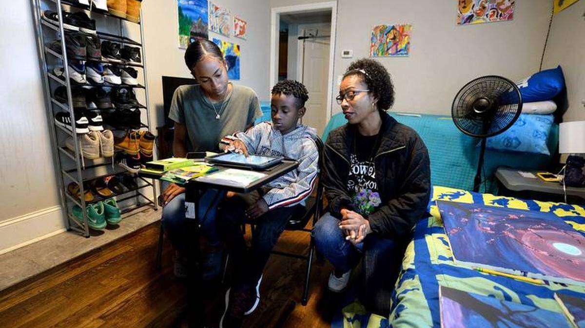 CMS parents are playing a large role in remote learning. Here, Daniel Feaster, center, does remote learning at home while his sister, D’erra Moise, left, and mother, Devonne Moise, watch. Daniel is a second-grader at Renaissance West STEAM Academy.