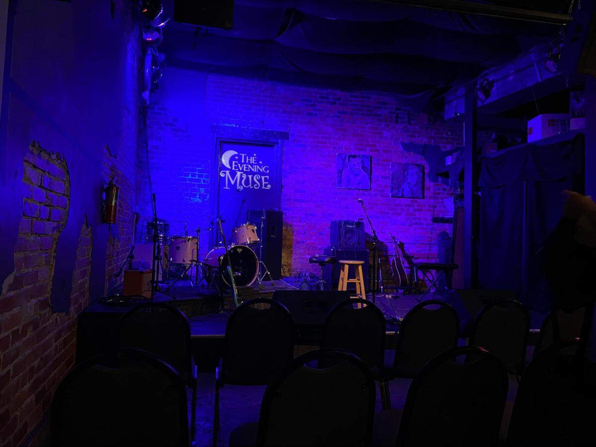 The stage is set for performers, and chairs await a full crowd at The Evening Muse.