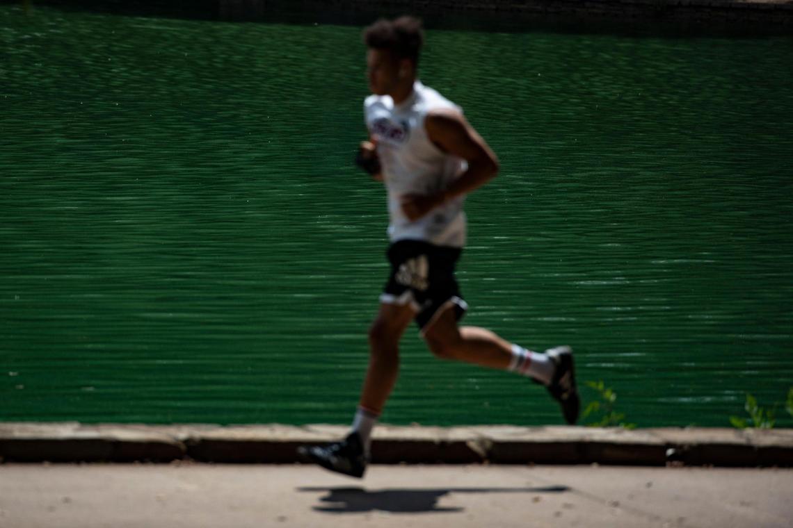 A park-goer jogs by the water where toxic blue-green algae has appeared at Freedom Park in Charlotte, N.C., on Wednesday, July 22, 2020.