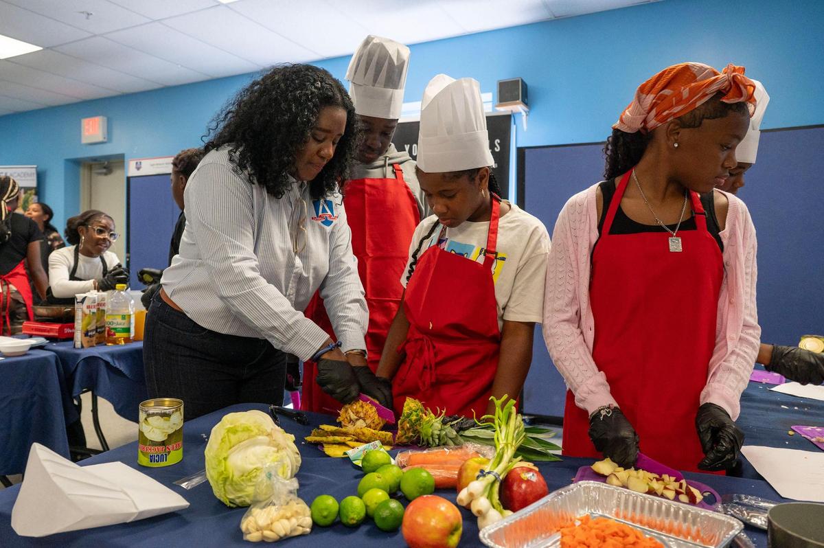 Laila Minott, superintendent and co-founder of A.C.E. Academy and Young Moguls, cuts up pineapple, with students, in preparation for their Jamaican-style dish during the ‘Can U Cook?’ cooking class segment of the Young Moguls’ Summer Camp at A.C.E. Academy in Harrisburg, NC, Tuesday June 17, 2025. A.C.E. Academy focuses on entrepreneurship with the Young Moguls program and connects the students with a variety of different careers through field trips and hands-on experiences.