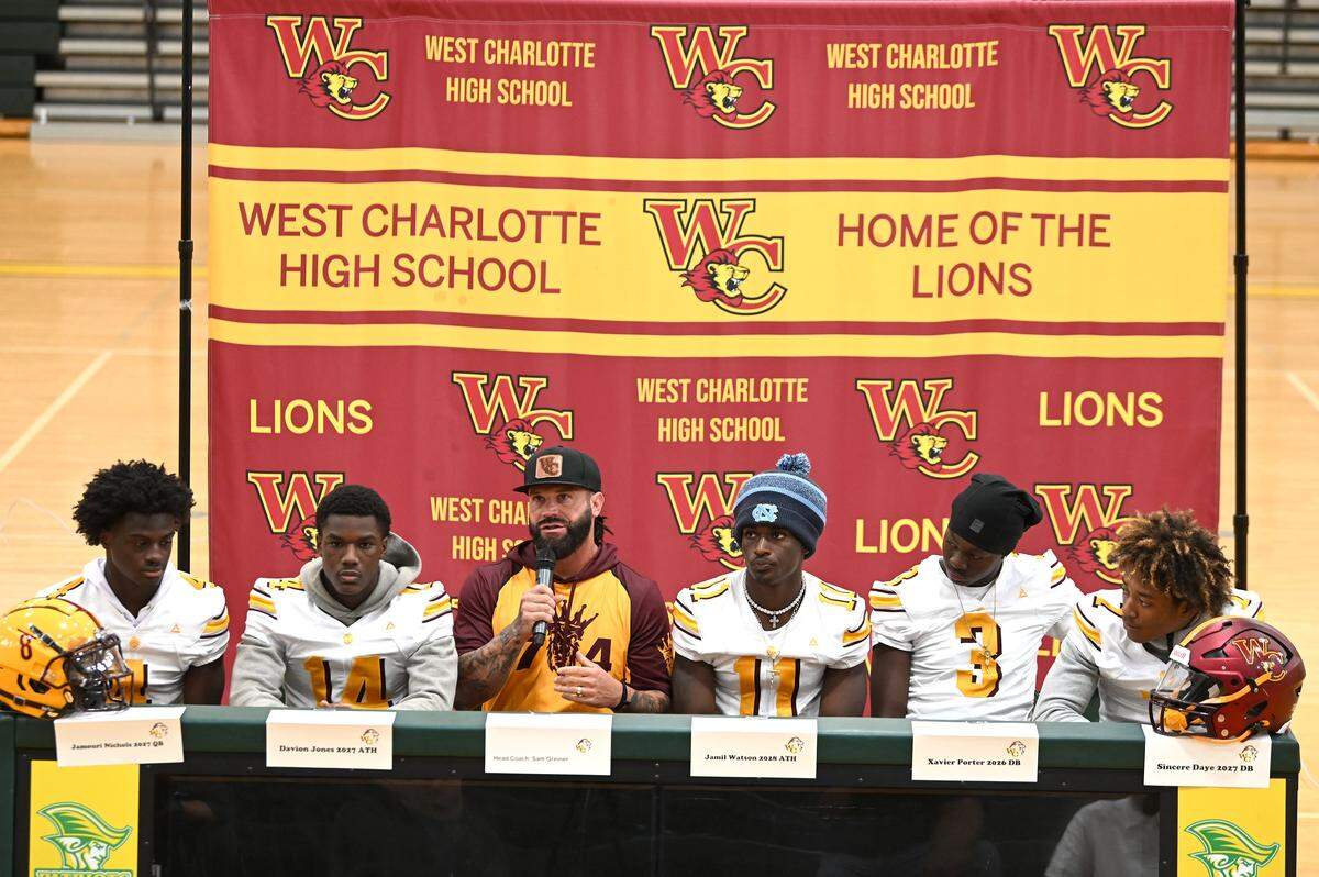 Flanked by members of his West Charlotte Lions football team, head coach Sam Greiner, center, responds to a question during the Mecklenburg County Power 6 media day on Tuesday, August 5, 2025 at Independence High School.