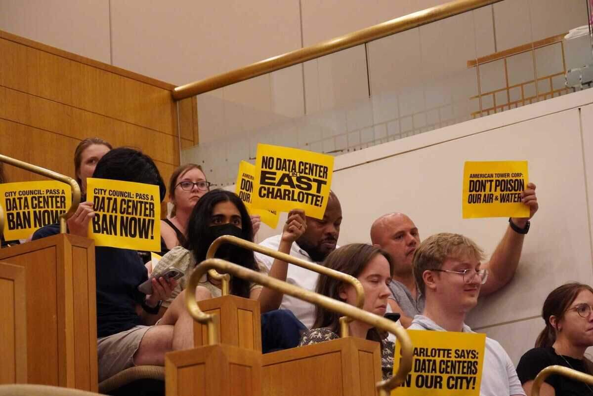 People in the audience of Monday’s Charlotte City Council meeting brought signs advocating against data centers, particularly one proposed in east Charlotte, before a unanimous vote in favor of a moratorium on new data center projects.