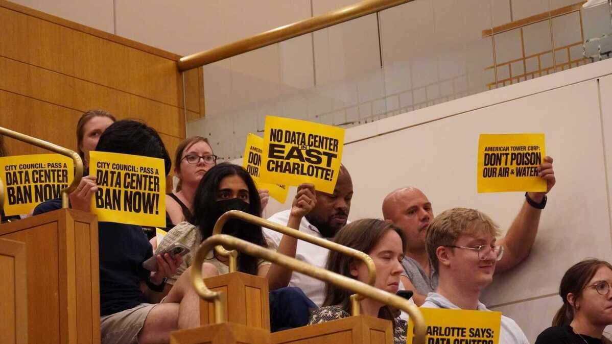 People in the audience of Monday’s Charlotte City Council meeting brought signs advocating against data centers, particularly one proposed in east Charlotte, before a unanimous vote in favor of a moratorium on new data center projects.