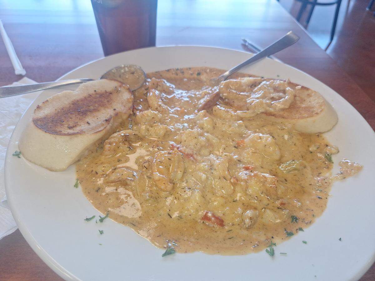 A white bowl of a creamy shrimp and grits dish, served with two pieces of toasted bread for dipping.
