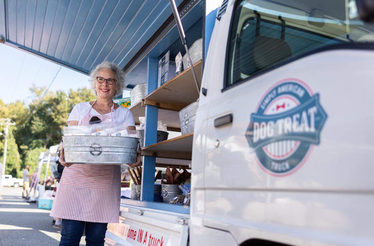 Amy Bossard holds a bin of treats by her food truck full of treats for dogs.