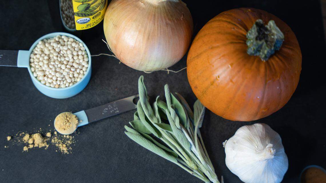 Ingredients for roast pumpkin soup on a cutting board, including a pumpkin, garlic, onion, sage, couscous and ground ginger.
