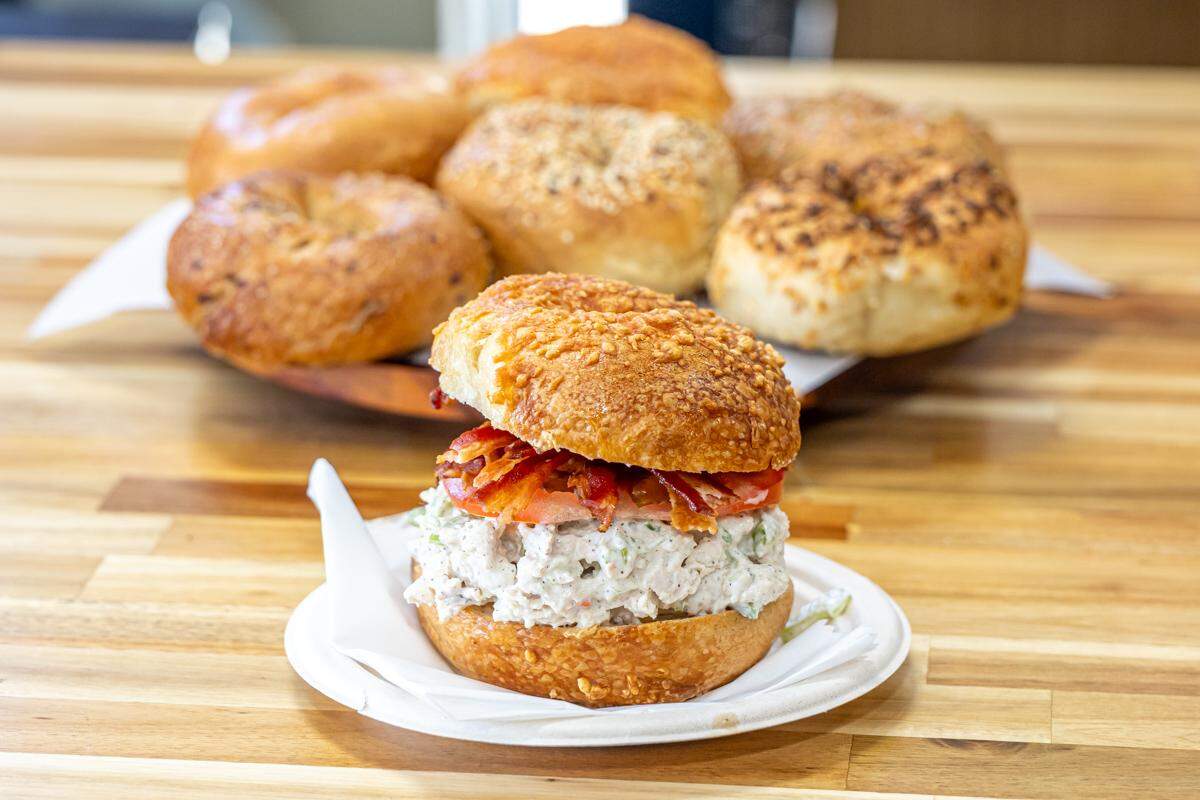 A bagel sandwich sitting on a white plate with plain and topped bagels blurred in the background.