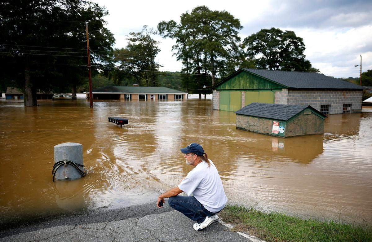 Dave Mooney crouches on the edge of the floodwaters in the neighborhood below Mountain Island Lake on Sept. 28, 2024.
