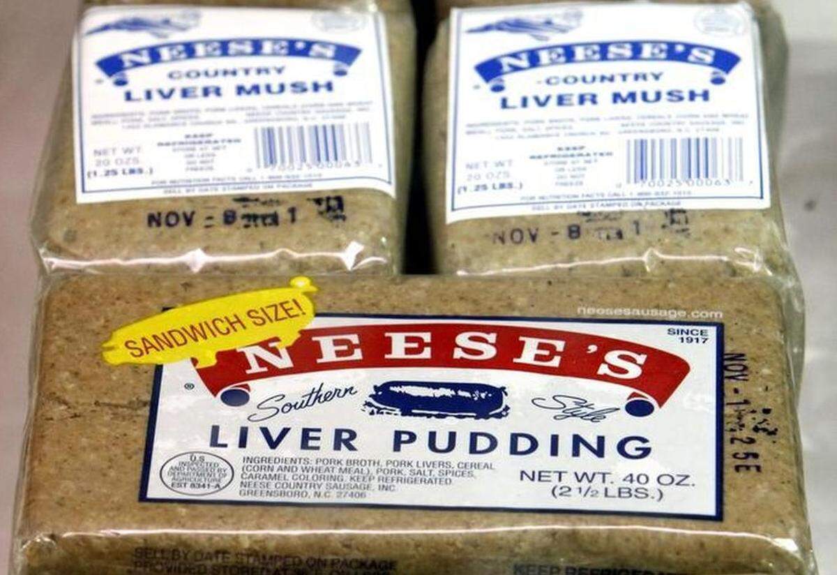 A close-up photograph of three refrigerated packages of Neese’s sausage products. Two smaller packages in the background are labeled ‘NEESE’S COUNTRY LIVER MUSH.’ A large package in the foreground is labeled ‘NEESE’S Southern Style LIVER PUDDING’ and has a yellow ‘SANDWICH SIZE!’ sticker adhered to the packaging.