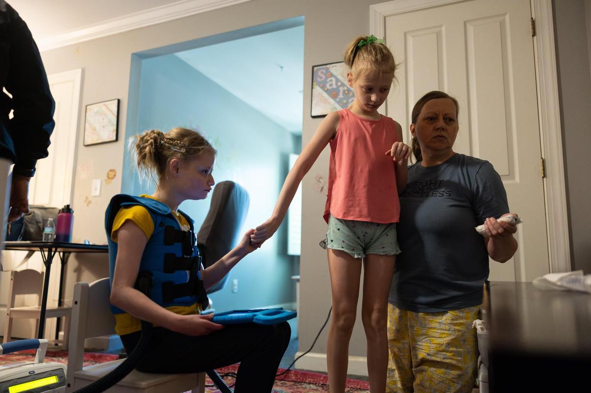 Stacy Staggs, turns on the T.V. as she helps her daughters, Emma, left, and Sara get ready in the morning in Charlotte, N.C., on Tuesday, April 11, 2025.
