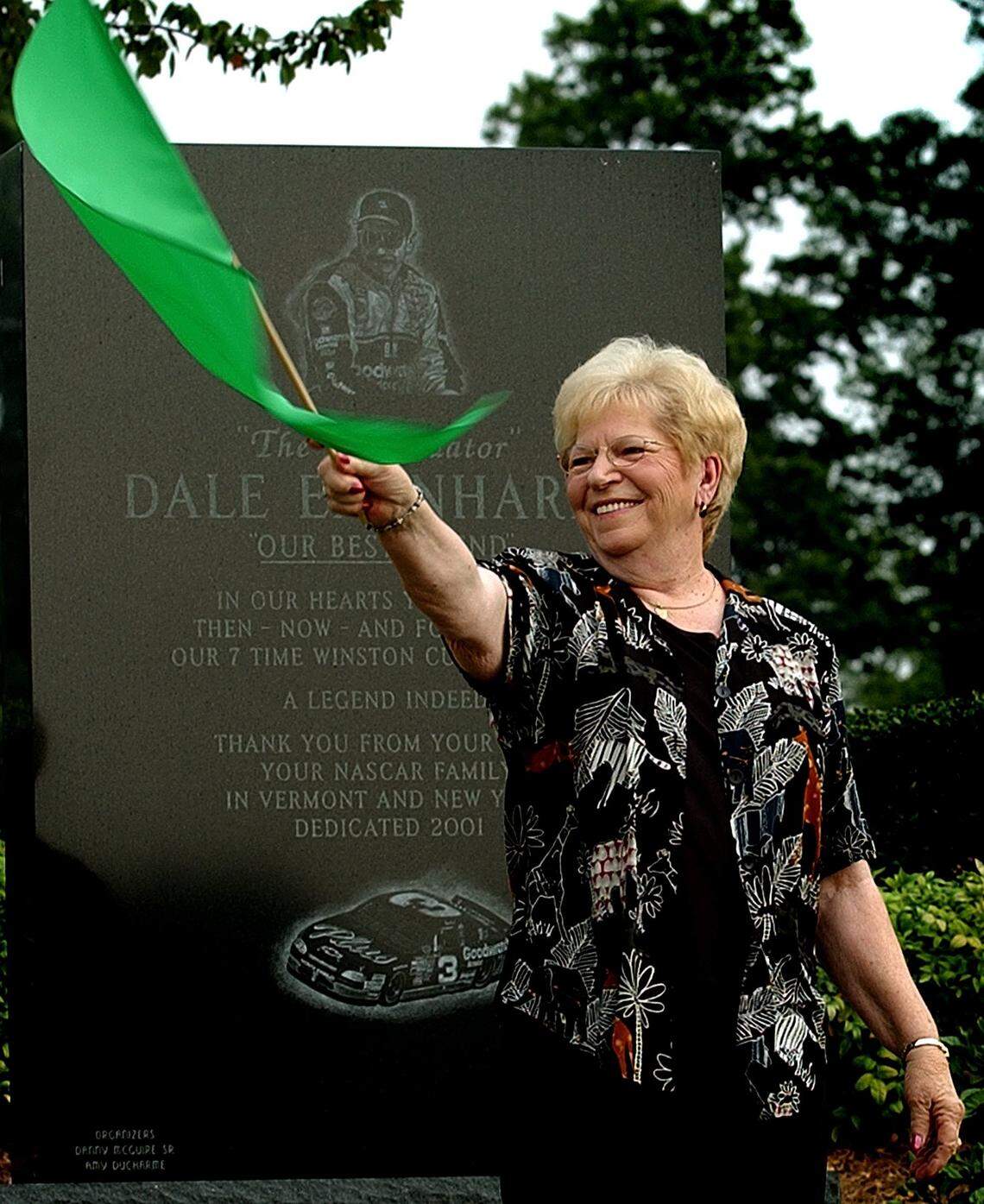 Martha Earnhardt, the mother of Dale Earnhardt Sr., waves the green flag to start the groundbreaking for the Dale Earnhardt Tribute Plaza on Aug. 21, 2002. The statue of her son, who died in the Daytona 500 in 2001, was unveiled two months later in October 2002. Martha Earnhardt is standing in front of a memorial that is also in the park, contributed by fans of Earnhardt from New York and Vermont.