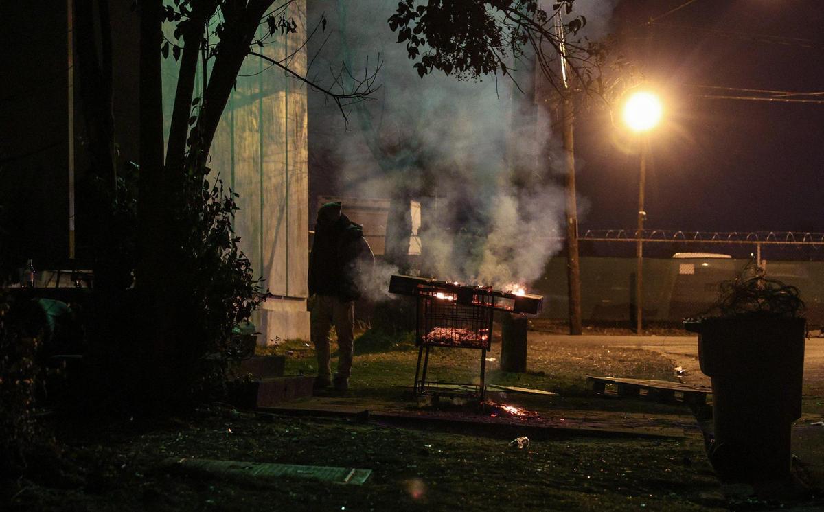 On Lucena Street, people experiencing homelessness, stand near a pallet burning in a shopping cart, trying to stay warm during the point in time count in Charlotte.