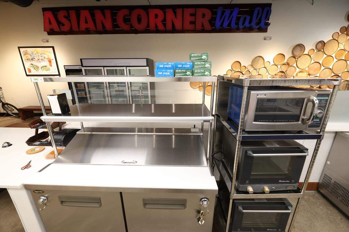 The new, unfurnished interior of a restaurant space, showing stainless steel prep tables, empty shelves and a rack of commercial ovens. A sign above reads Asian Corner Mall in red and blue letters.